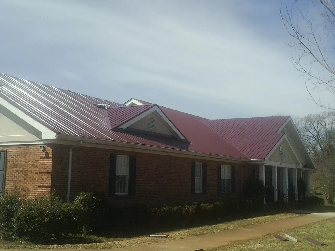 Red metal roof with gabled entries on a long brick building, from a Hail Damage Roof Repair job in Homosassa