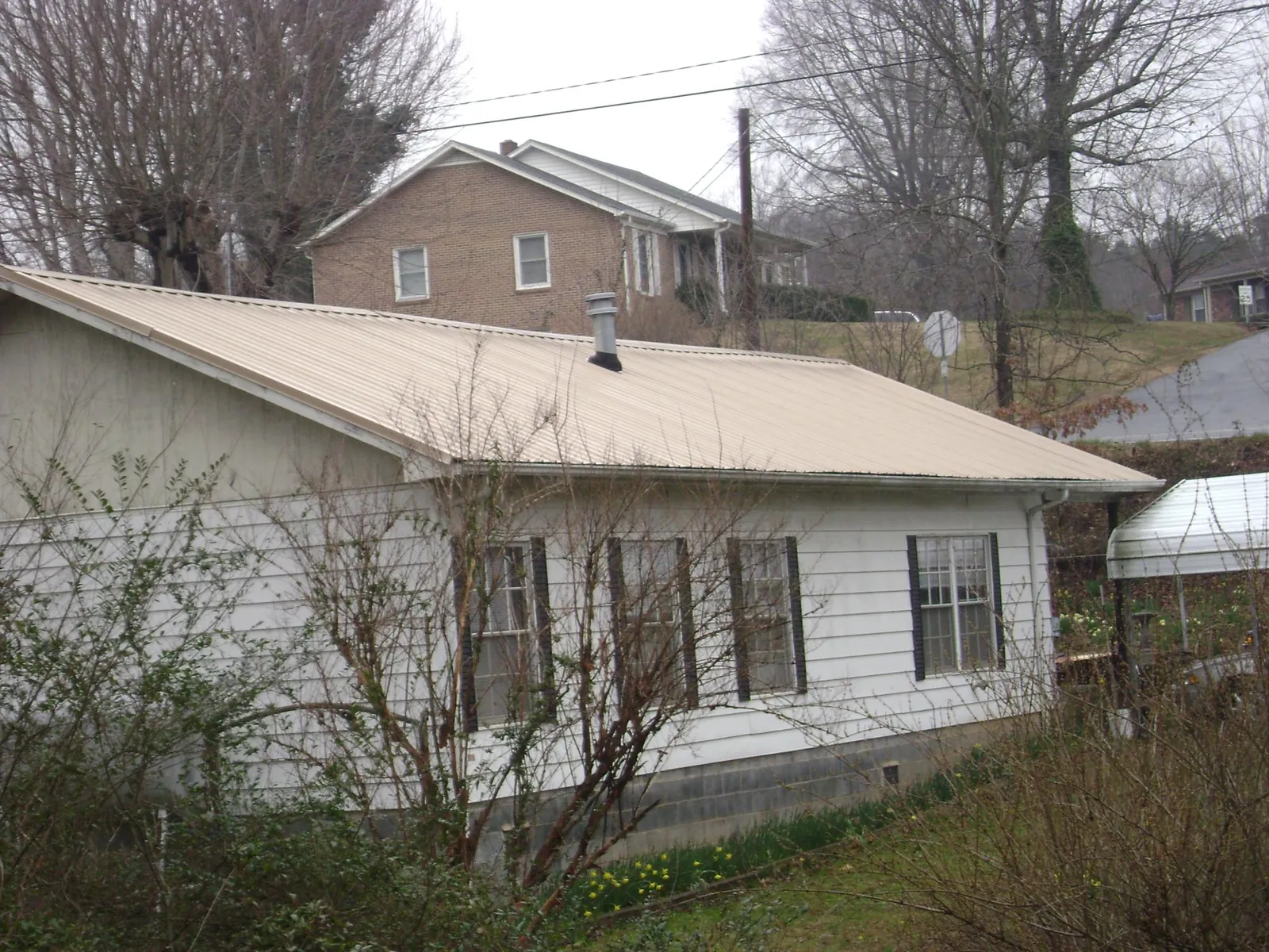 Tan metal roof on a white sided house set into a hillside — Commercial Roofing by Roofing Brothers in Homosassa